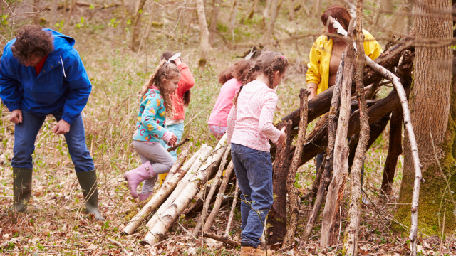 A group of children making a shelter in woodland with supervising adults