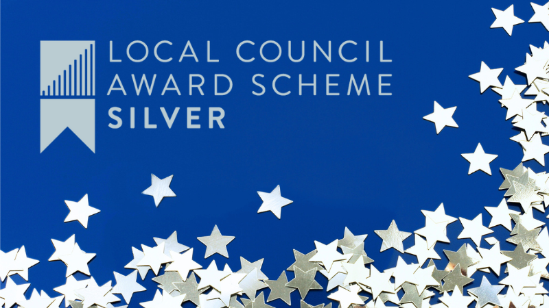 Dark blue background with metallic silver stars scattered across bottom and right side. Logo for Local Council Award Scheme Silver in top left